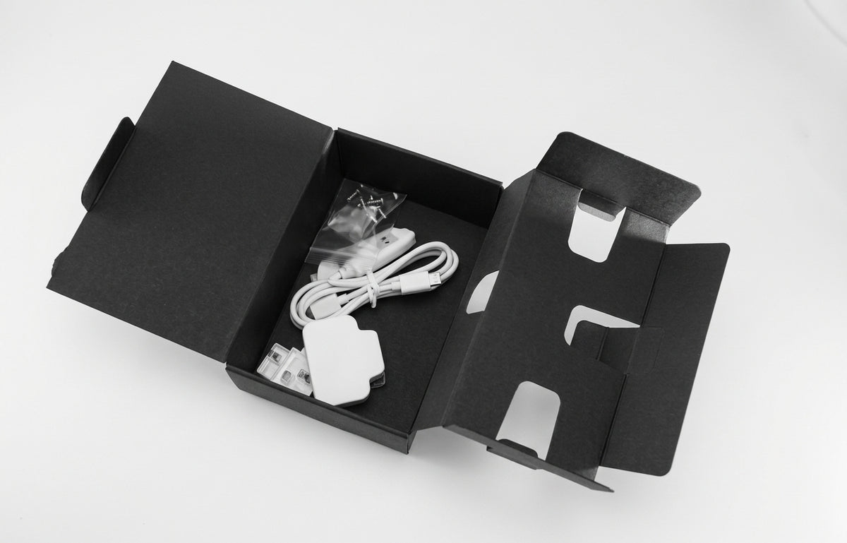 Black textured one-piece carton for handsets, size 3, opened out with a charger and cable inside